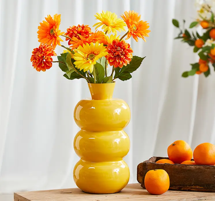 Vase af jern i gul vist med kunstige gerbera og dahlia i gule og orange farver