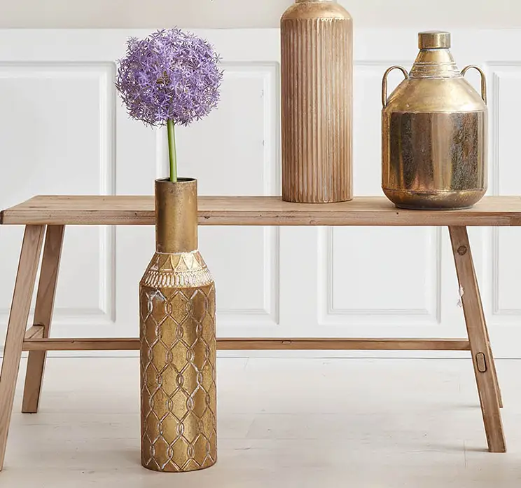 Kunstig prydløg i lilla sat i fin metal vase i guldfarvet på gulv i stue