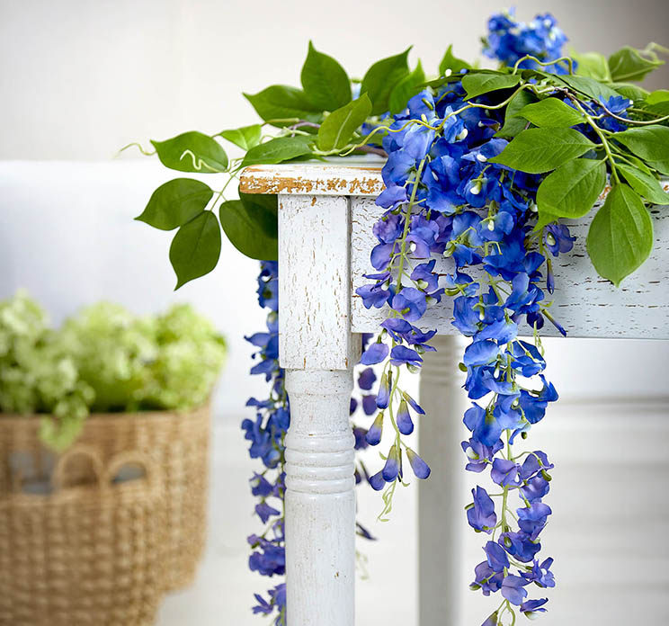 Wisteria også kaldet blåregn kunstig blomst af plast i blå vist liggende på et træbord