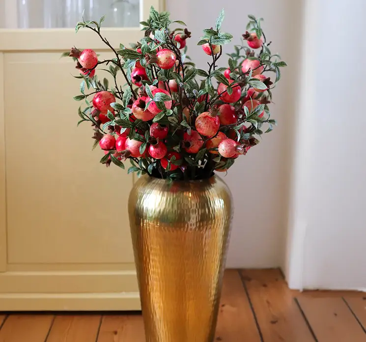 Granatæble kunstig grene af plast i rød og gul, flere sat sammen til en frugt buket i vase på gulv