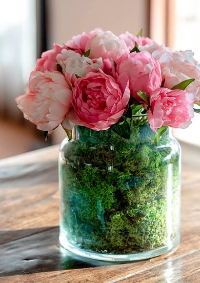 Lyserøde peoner i glas vase med grøn mos