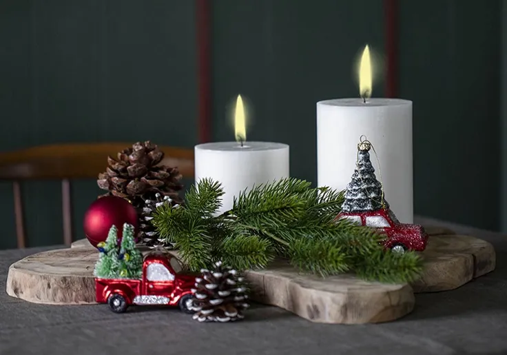 Juledekoration med julebiler, kunstig gran og stearinlys på træskive