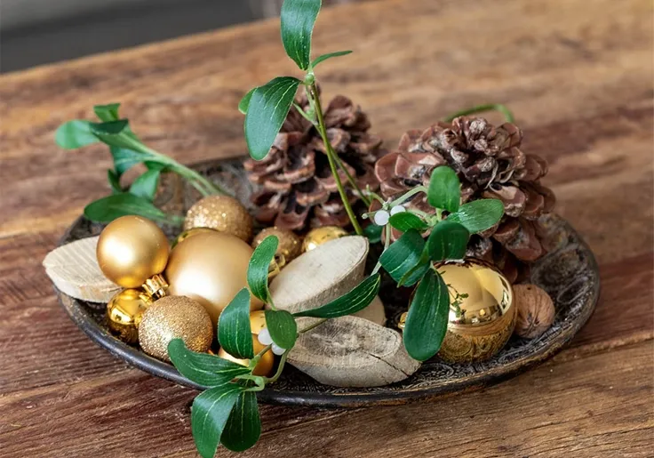 Juledekoration med guldkugler, kunstig mistelten, ægte kogler og træskiver på fad