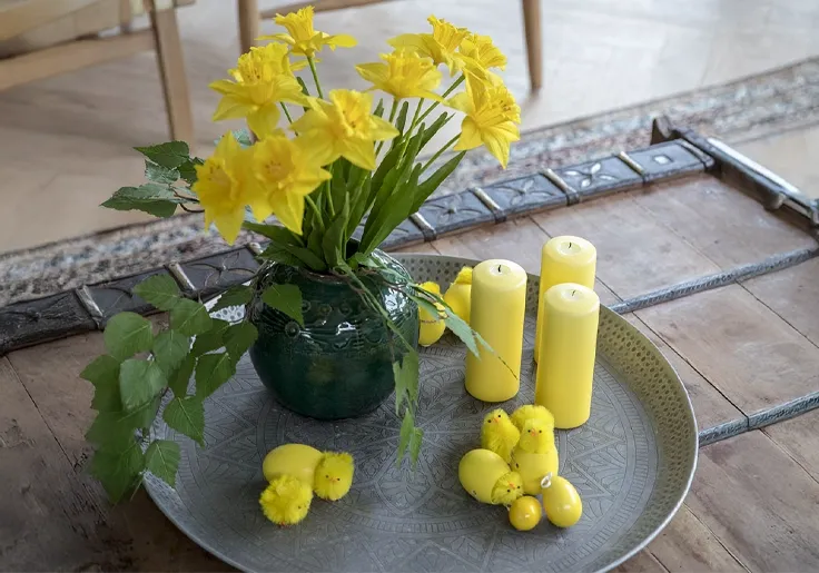 Kunstige påskeliljer og påskekyllinger på fad med lys til dekoration
