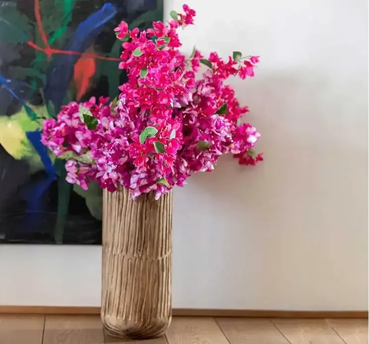 Kunstig bougainvillea blomst i pink af plast vist i en høj vase af træ på gulv