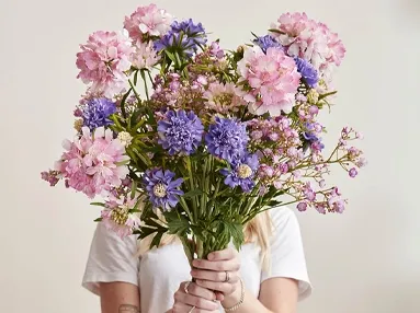 Blandet buket af kunstige blomster som kornblomster, brudeslør og skabiosa i lilla og lyserøde blomster.