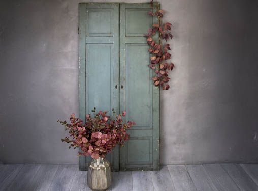 trædør pyntet med kunstig hængende efterårsgren, og vase i banket metal med efterårsgrene er sat nede foran døren