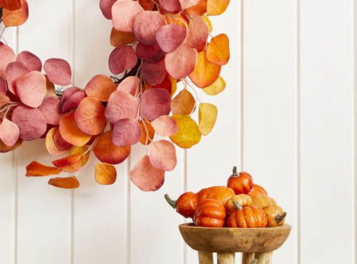 kunstig eukalyptus krans i orange farver og en lille træskål på fødder fyldt med små forskellige kunstige græskar