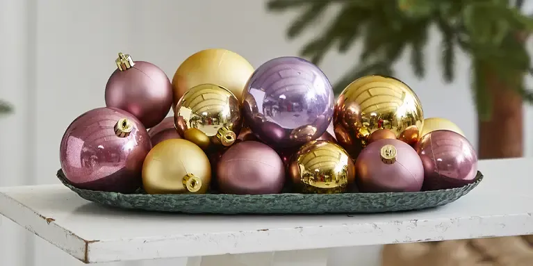 blandede plast julekugler i rosa, lilla og guld på fad