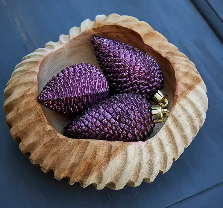 Julepynt grankogler af plast i lilla med glimmer vist på bord i en træskål