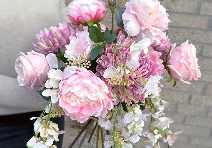 Smuk lyserød buket af kunstige blomster som pæoner, krysantemum, roser, texasklokker og wisteria