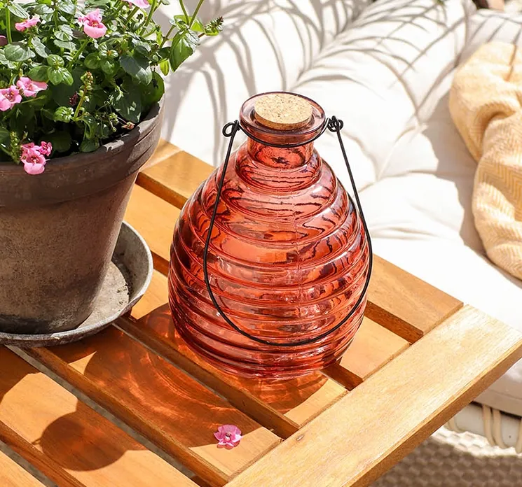 dekorativ hvepsefanger i orange af glas og med korkprop sat på havebord