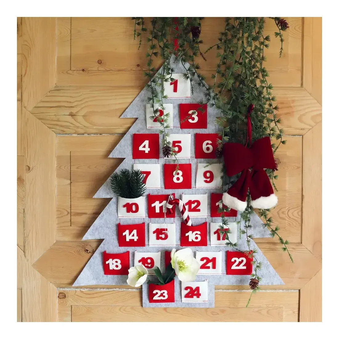 Julekalender af polyester med 24 små lommer til gaver vist hængende på dør med små ting