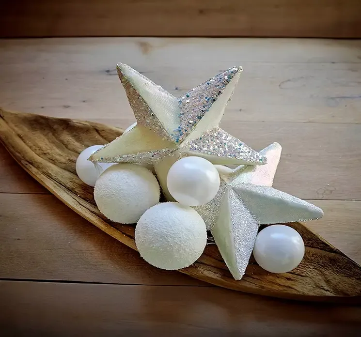 Julepynt stjerner til ophæng vist i aflangt træfad med kunstige snebolde på et bord