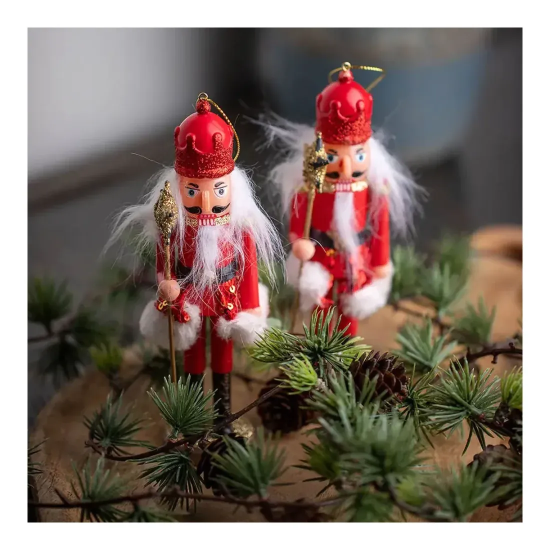 Nøddeknækker af plast i rød med ophæng julepynt vist i miljø med kunstig gran