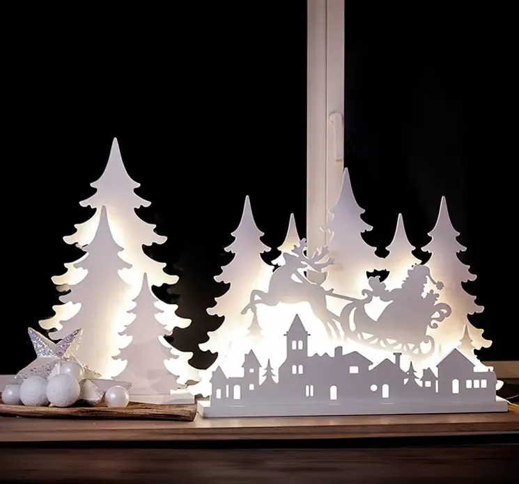 Julescene i hvid af plast med lys vist i vindue om aftenen med tændt lys