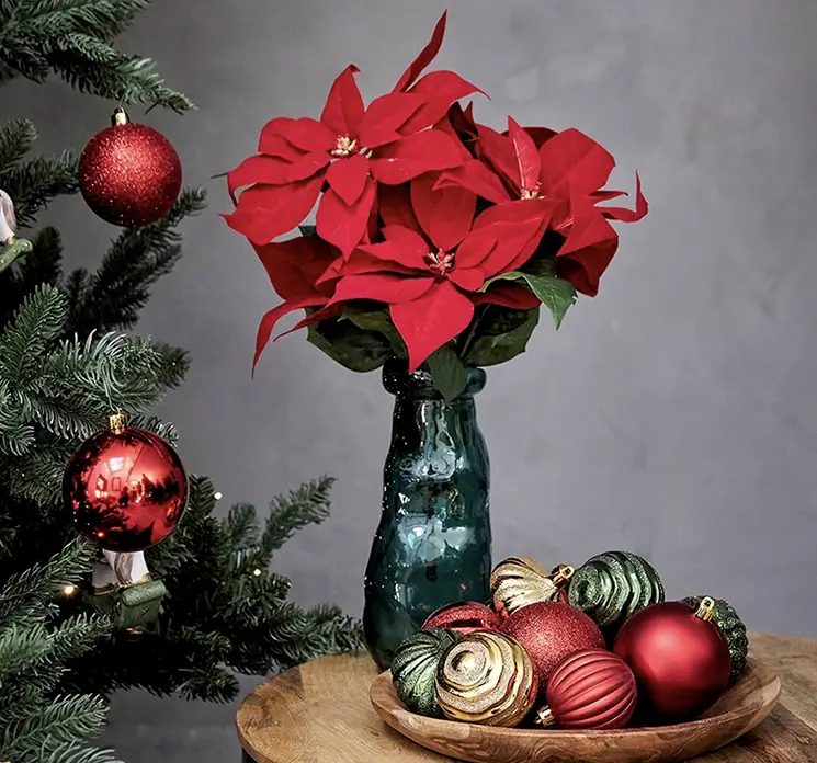 Julestjerne kunstig blomst i rød sat i simplicity glasvase i julemiljø med blandede julekugler af plast