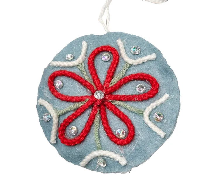 Filt kugle i blå med pynt på en side, kuglen er flad og med snor til at hænge op