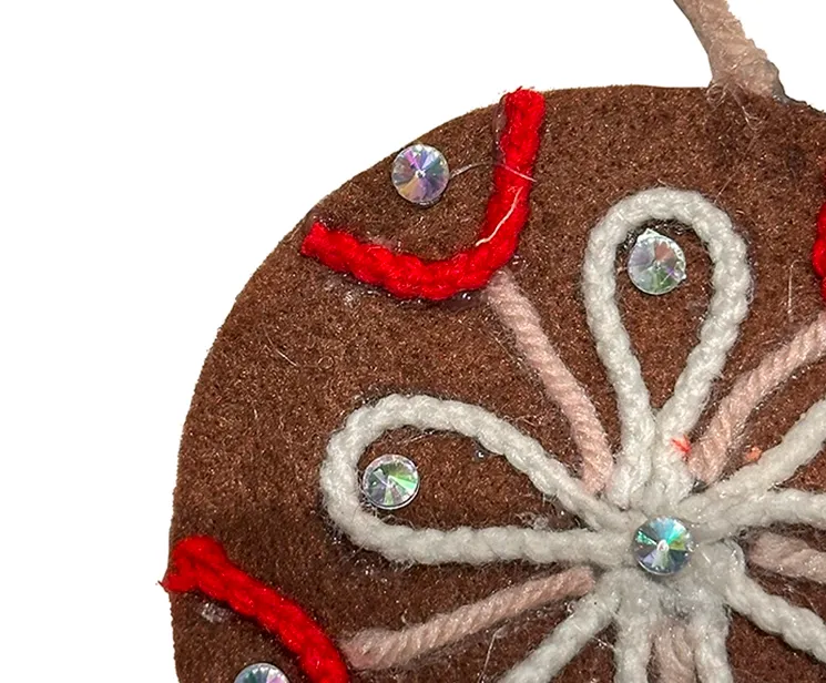 Filt kugle i brun med pynt på en side, kuglen er flad og med snor til at hænge op closeup