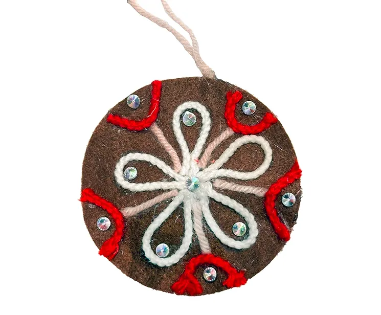 Filt kugle i brun med pynt på en side, kuglen er flad og med snor til at hænge op