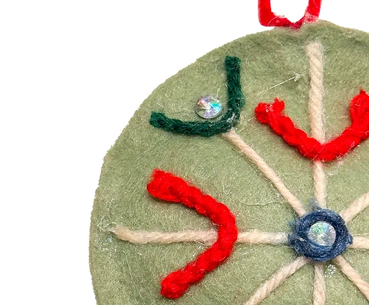 Filt kugle i grøn med pynt på en side, kuglen er flad og med snor til at hænge op closeup