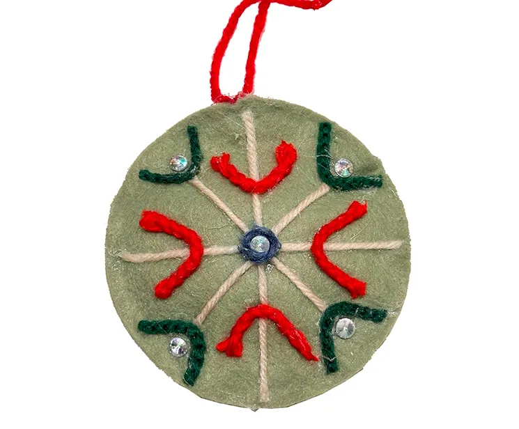 Filt kugle i grøn med pynt på en side, kuglen er flad og med snor til at hænge op