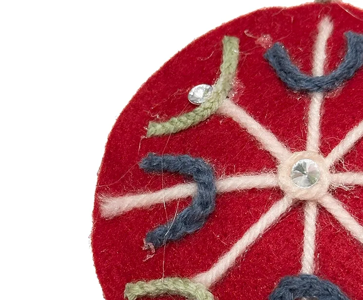 Filt kugle i rød med pynt på en side, kuglen er flad og med snor til at hænge op closeup