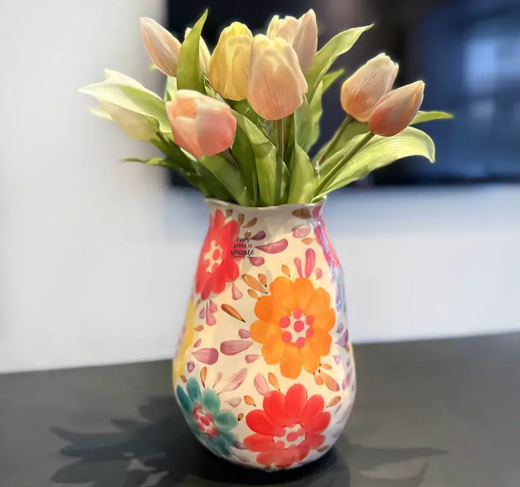 Vase af håndlavet keramik med påmalede blomster her vist med en buket kunstige tulipaner på sofabord