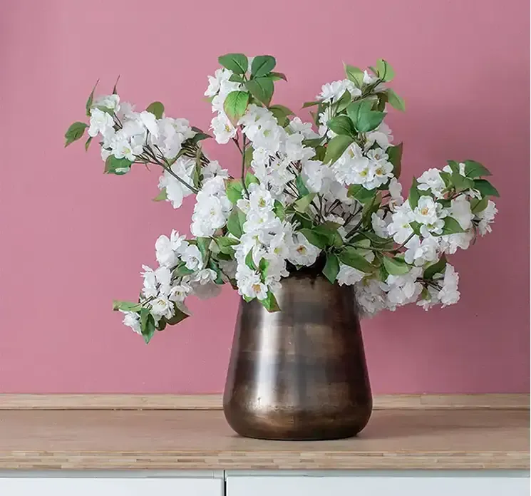 Kunstige æblegrene med hvide blomster af plast sat i vase på køkkenbord