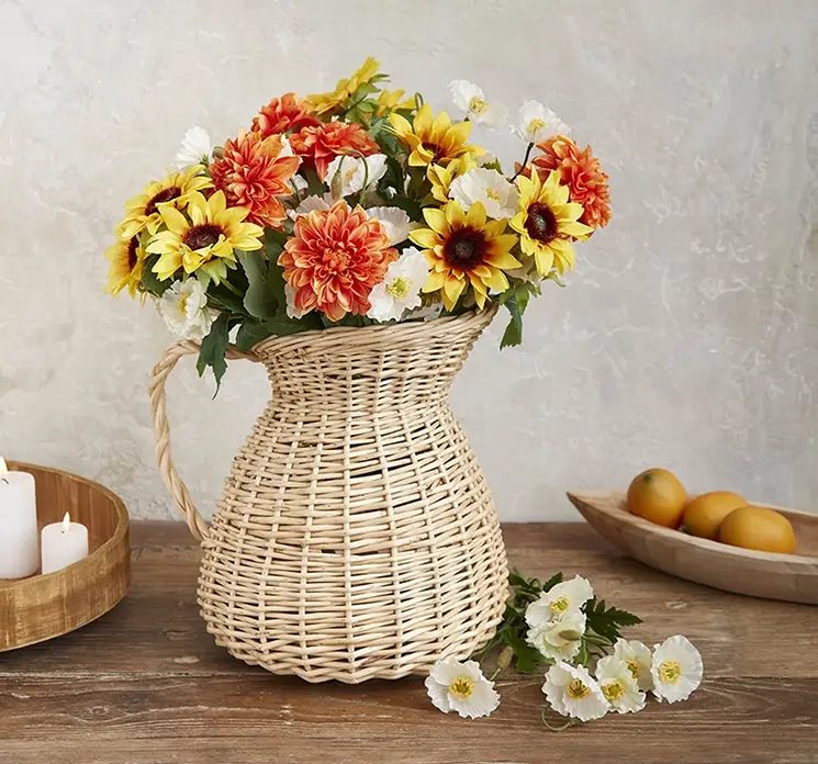 Valmuebuket af kunstige blomster af plast i hvid vist i flettet vase med flere andre blomster på spisebord