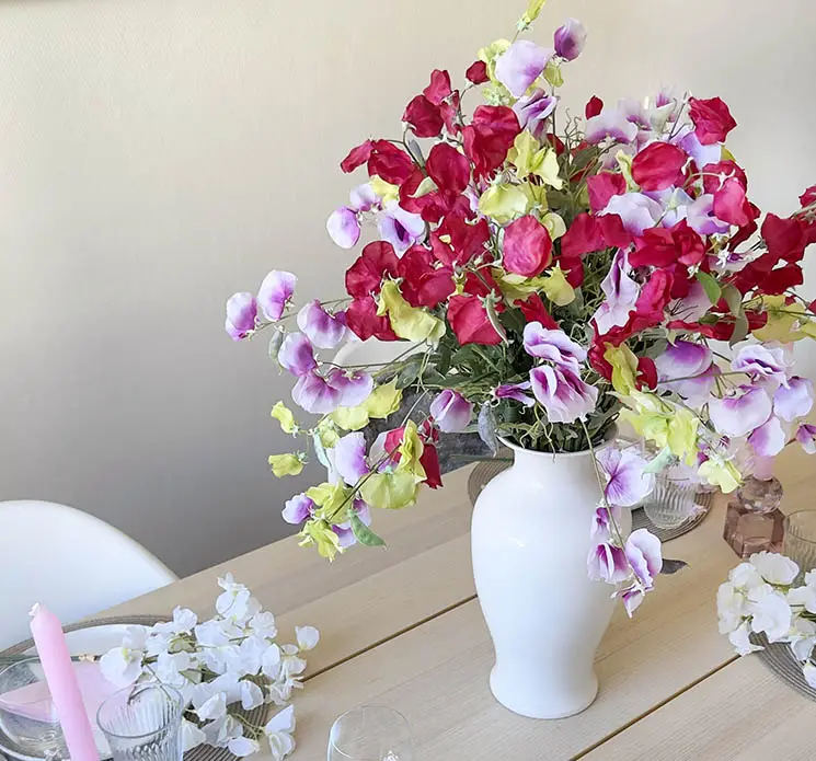 Vase af metal i hvid vist på spisebord med kunstige ærteblomster