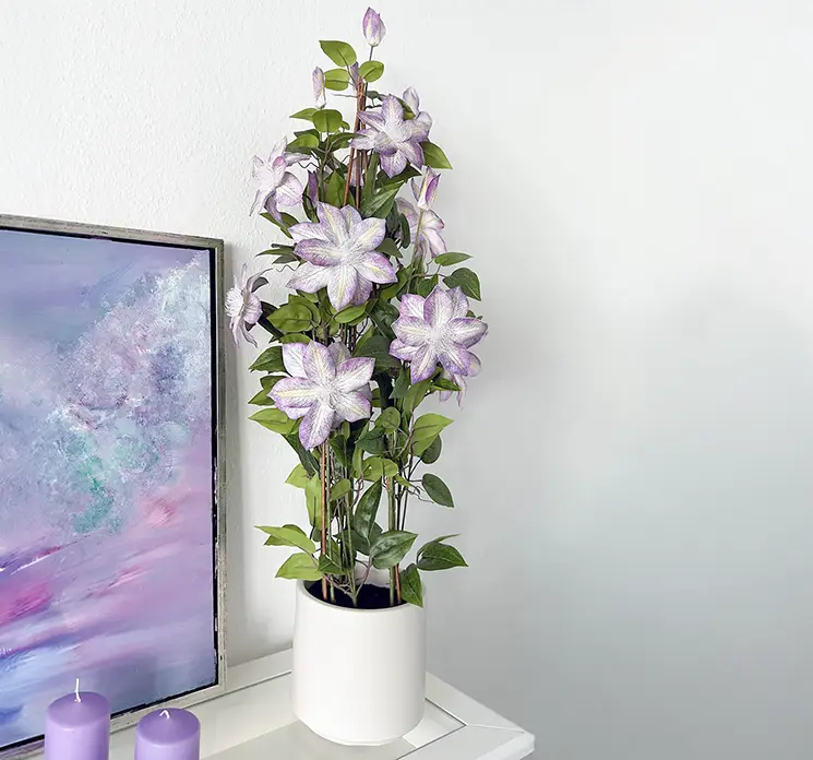 Klematis kunstig blomst i lilla af plast og med hvid potte vist i stuemiljø