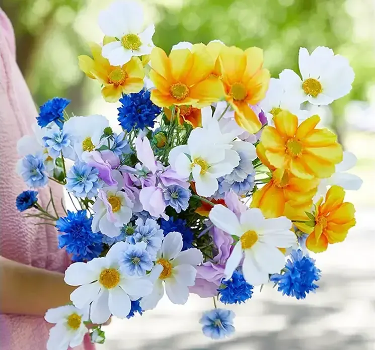 Kunstig kornblomst i blå vist i en buket sammen med andre kunstige blomster i gule, hvide og blå nuancer
