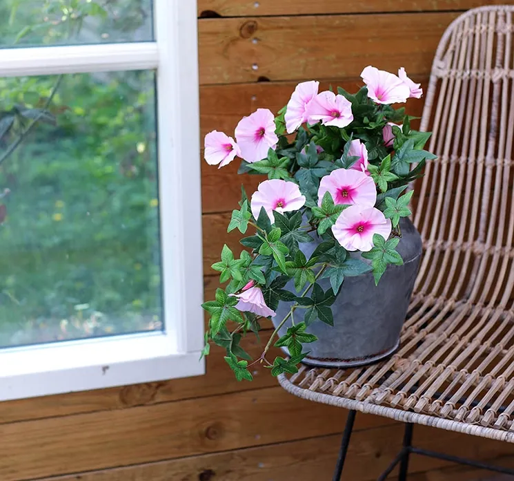 kunstig lyserød petunia hænger sat i en rund zinkvase på havemøbel