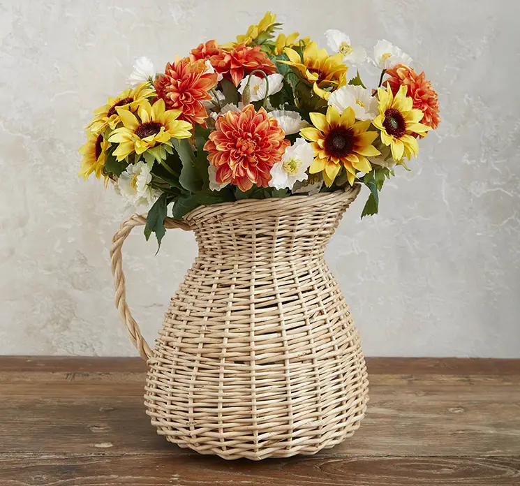 Solsikke kunstig blomst vist i flettet vase kande med andre kunstige blomster som dahlia og valmuer på træbord