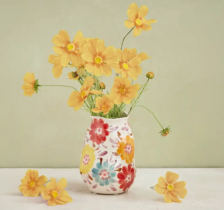 Stolt kavaler kunstig blomst i gul af plast vist i blomstret vase på bord