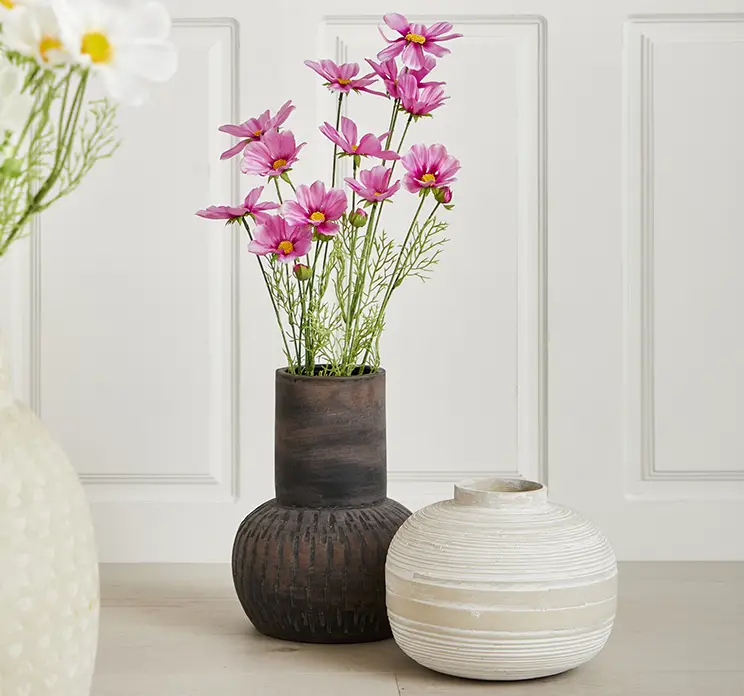 Stolt kavaler af plast i pink kunstig blomst vist i terracotta vase i stuemiljø