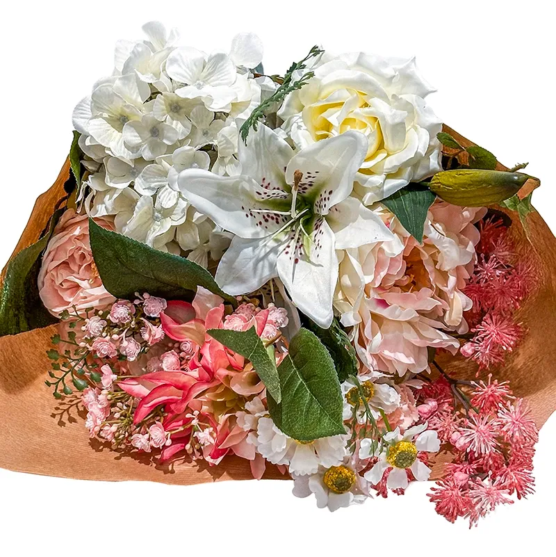 Smuk kunstig buket i hvide og lyserøde farver af forskellige kunstige blomster pakket fint ind i blomsterpapir closeup