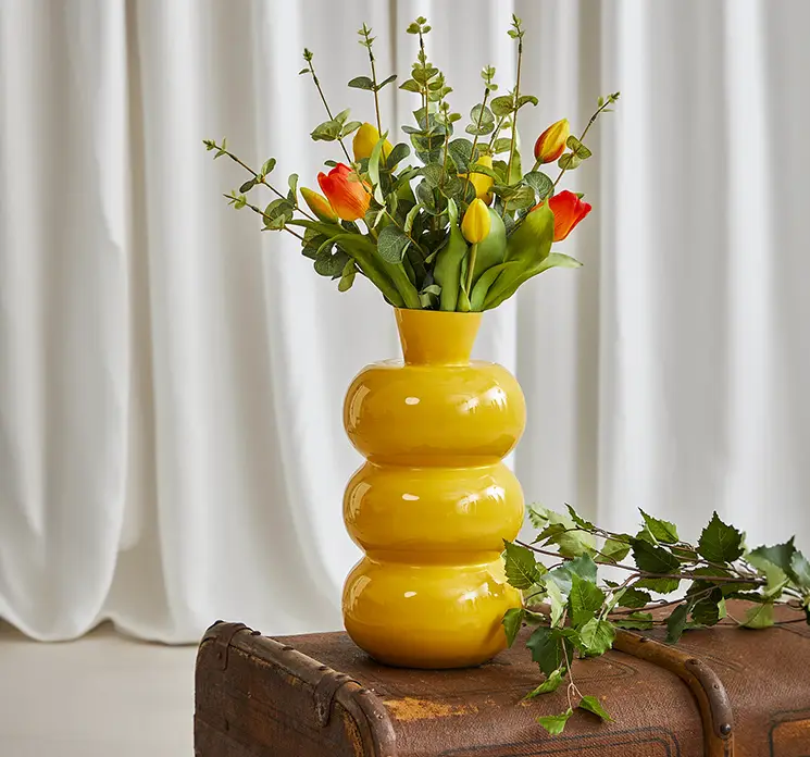 Tulipan buket med kunstige blomster i gule og orange farver af gummi sat i gul vase med kunstig eukalyptus i stuemiljø