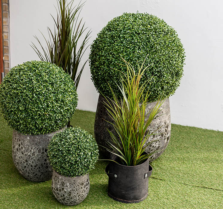 Kunstig buksbom bold i grøn uv-beskyttet vist i havemiljø