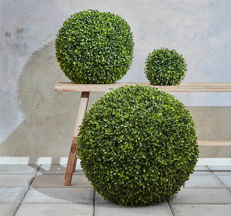 Kunstig buksbom bold af plast i grøn vist på terrasse med andre størrelser