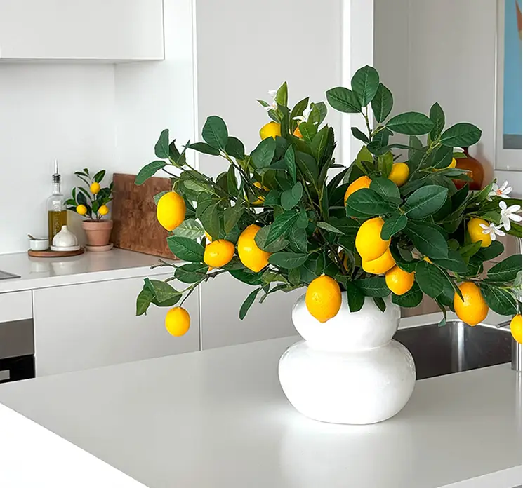 Citron grene kunstige med citroner af plast i gul og grøn sat sammen i hvid vase på køkkenbord