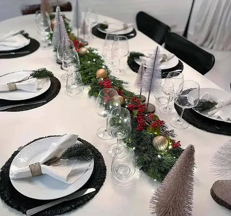 Kunstig børste juletræ af plast i brun på rund træfod vist på et julebord med kunstig granranke og julekugler