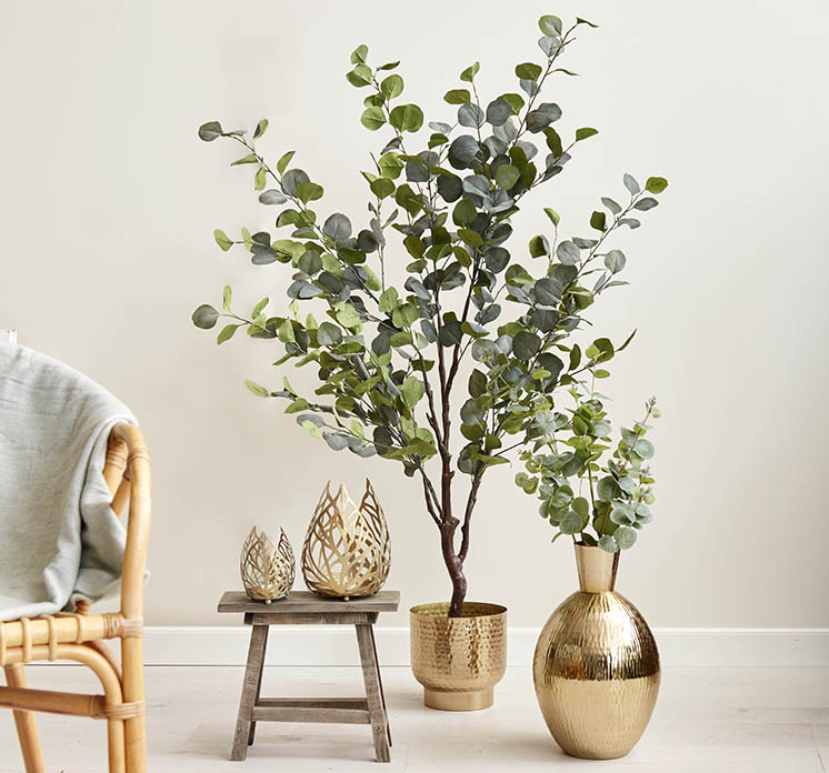 Kunstig eukalyptus træ i potte af plast vist i miljø med guld farvet potte