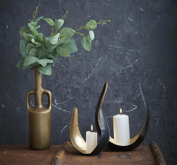 Lysestager med skulpturelt look af metal i sort og guld farvet vist i stuemiljø med bloklys
