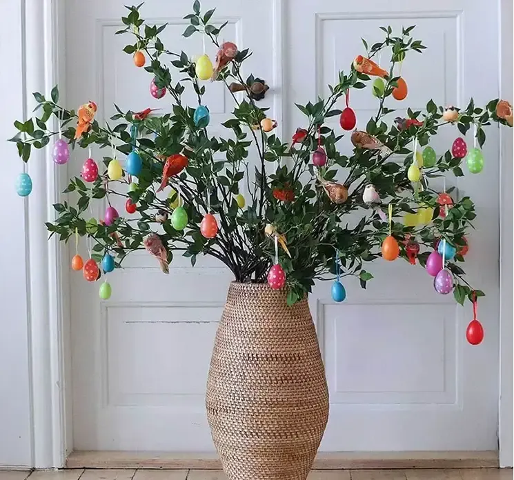 Vase af rattan i natur farver vist med kunstige grene og påskeæg af plast i mange farver