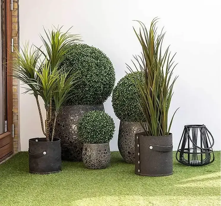 Græs i sort potte af plast kunstig græs vist i havemiljø med andre kunstige uv-beskyttede planter