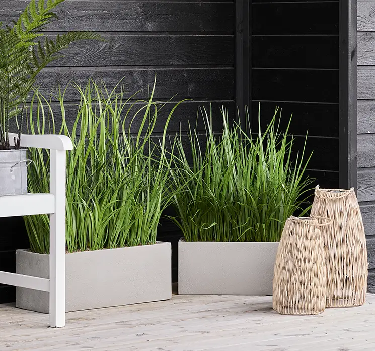 Græs kunstig af uv-beskyttet plast i grøn med plantekasse vist på terrasse med lanterner