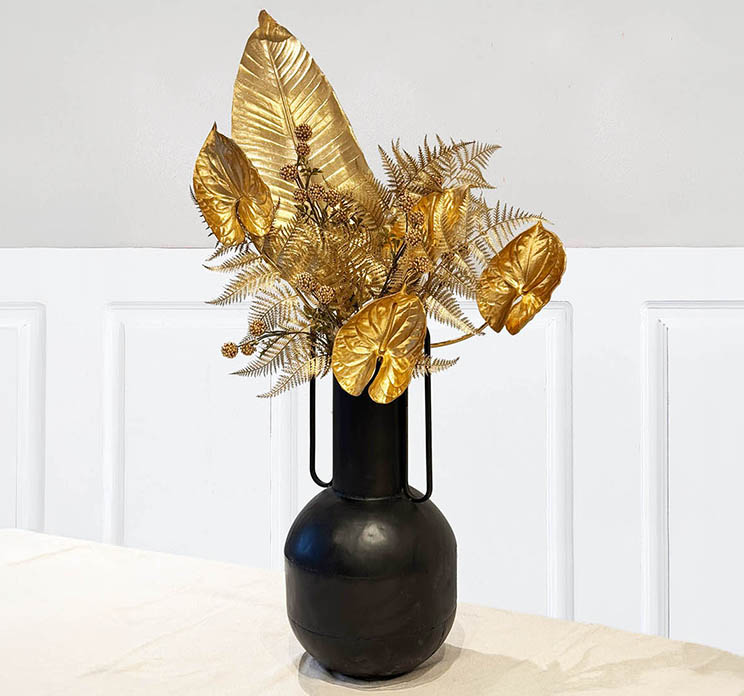 Forskellig kunstige grene og blomster i guldfarvet sat i en metal vase i sort