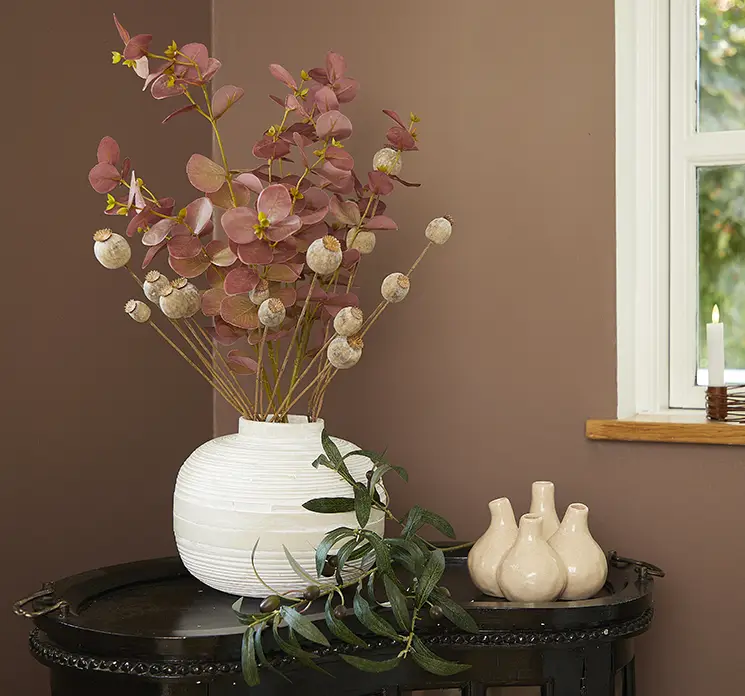 Eukalyptus kunstig gren af plast i rosa farvet 86cm sat i en bambus vase i hvid med valmuefrøkapsler på lille sidebord